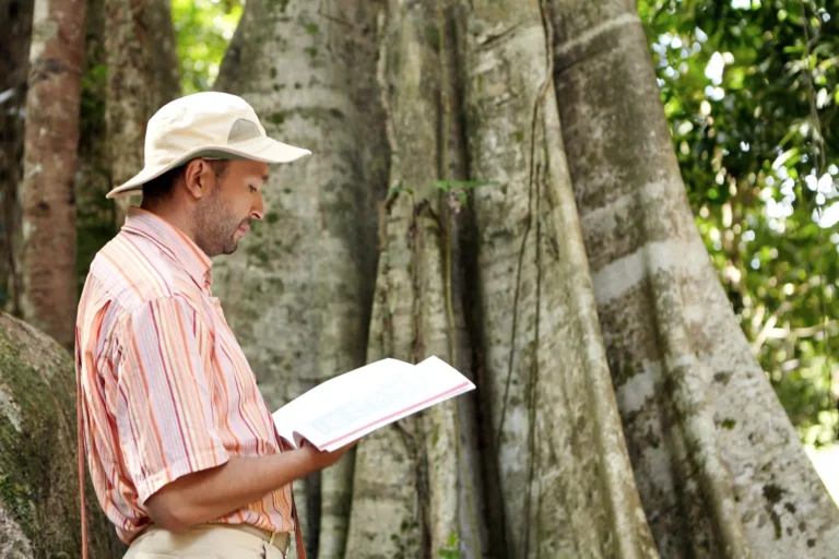 side-view-caucasian-male-botanist-panama-hat-striped-shirt-exploring-species-field-work-tropical-forest-standing-front-big-plant-reading-information-emergent-tree-manual