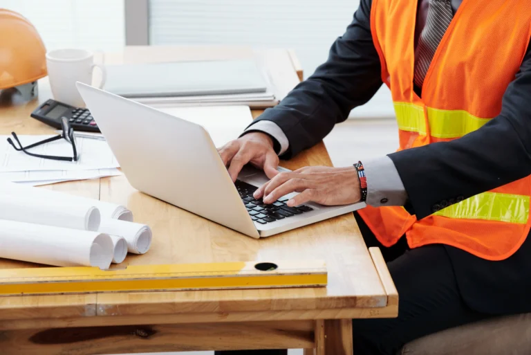 unrecognizable-man-neon-safety-vest-business-suit-sitting-desk-using-laptop Image description